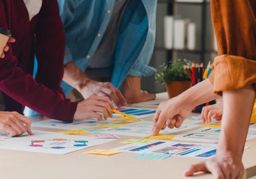 Asian businessmen and businesswomen meeting brainstorming ideas about creative web design planning application and developing template layout for mobile phone project working together in small office.